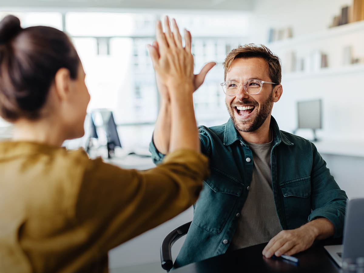 Zwei Personen geben sich in einem Büro lächelnd ein High Five als Zeichen erfolgreicher Zusammenarbeit.