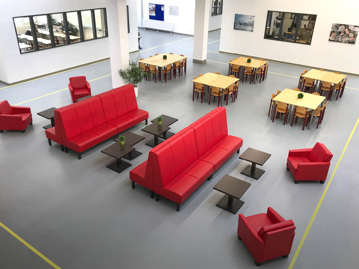 Der Aufenthaltsraum des ZAW: Eine Halle mit neutralem Boden, Sitzgruppen mit roten Sofas und kleinen Tischen, im Hintergrund größere Tische mit Stühlen.