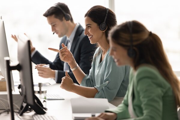 Diverse Kundenbetreuungsteams sitzen am Schreibtisch in Headsets und kommunizieren online über Computer, die Kundenbeziehungen verwalten und Anfragen bearbeiten.