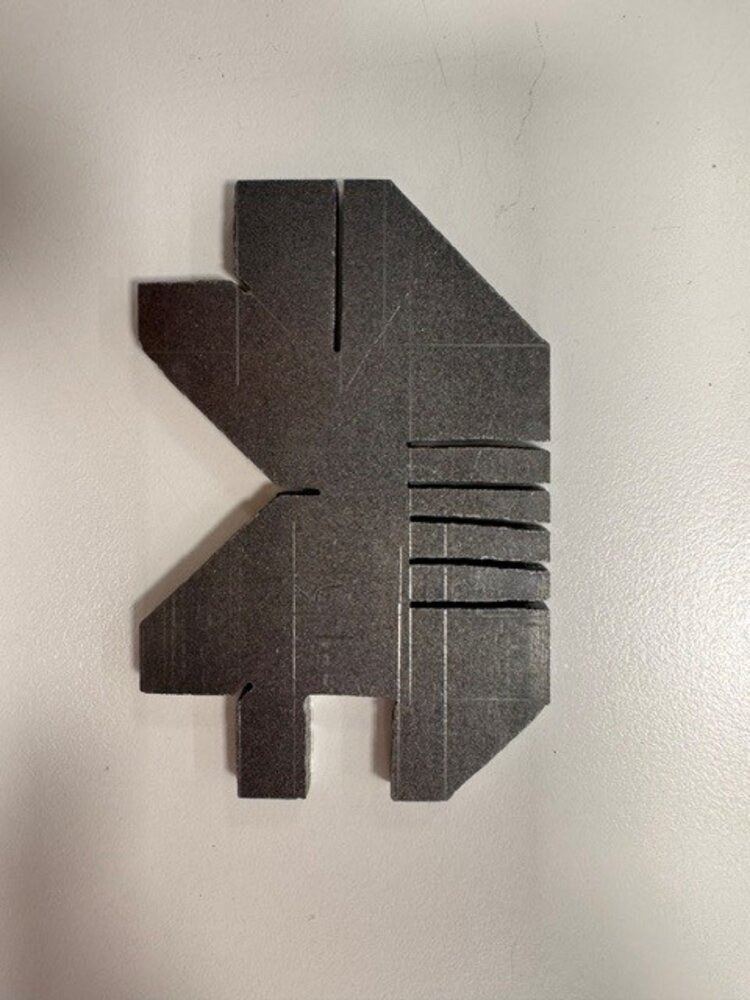 Dunkles, unregelmäßig geformtes Metallwerkstück mit verschiedenen Aussparungen, Abstufungen und mehreren parallel eingeschnittenen Schlitzen auf der rechten Seite.