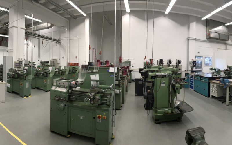 Weitläufige Metallwerkstatt mit zahlreichen grünen Dreh-, Fräs- und Bearbeitungsmaschinen sowie Werkzeugschränken und Arbeitsplätzen.