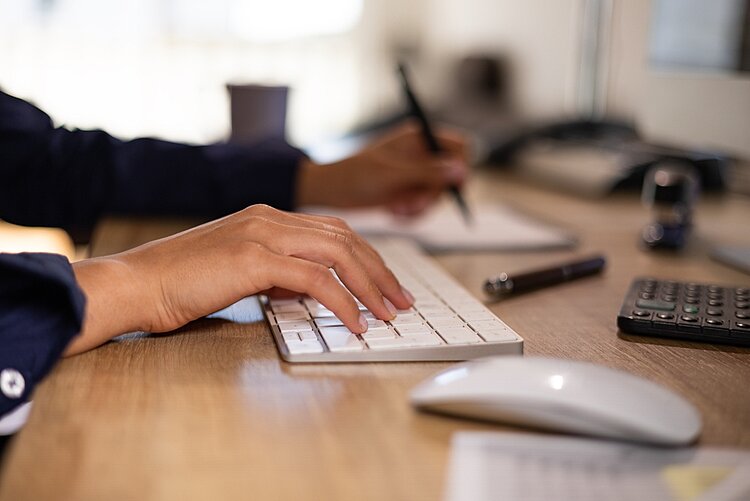 Eine Person, von der nur die Hand zu sehen ist, arbeitet an einem Computer.