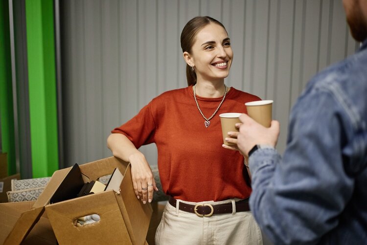 Eine junge erwachsene Frau diskutieren mit einem Mann, während beide Kaffee trinken und verpackt Boxen neben ihnen stehen.