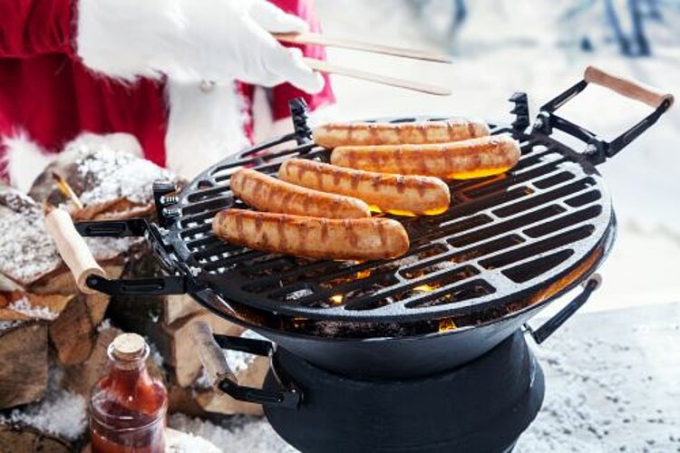 Weihnachtsfeier der Auszubildenden Ein Weihnachtsmann grillt Würstchen auf einem runden Grill im Schnee.