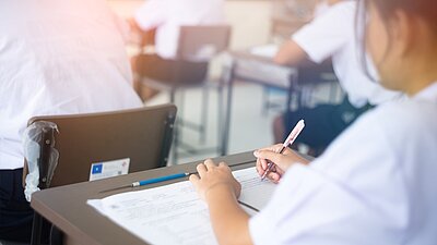 Eine junge Frau sitzt an einem Tisch und schreibt eine Prüfung