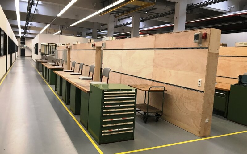 Reihe von Werkbänken in einer Ausbildungswerkstatt, ausgestattet mit Werkzeugschränken, Stromanschlüssen und Arbeitsplätzen.