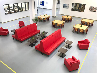 Der Aufenthaltsraum des ZAW: Eine Halle mit neutralem Boden, Sitzgruppen mit roten Sofas und kleinen Tischen, im Hintergrund größere Tische mit Stühlen.