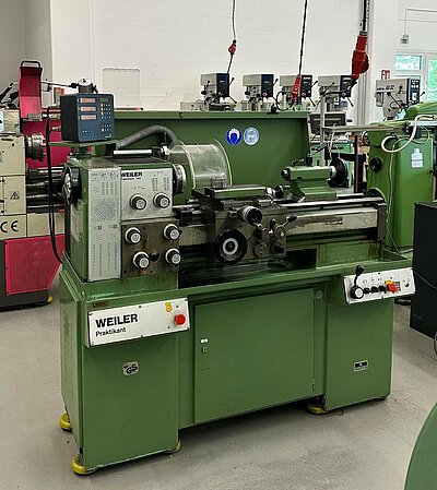 Grüne Drehmaschine vom Typ „WEILER Praktikant“ in einer Ausbildungswerkstatt für Metallbearbeitung, umgeben von weiteren Werkzeugmaschinen.